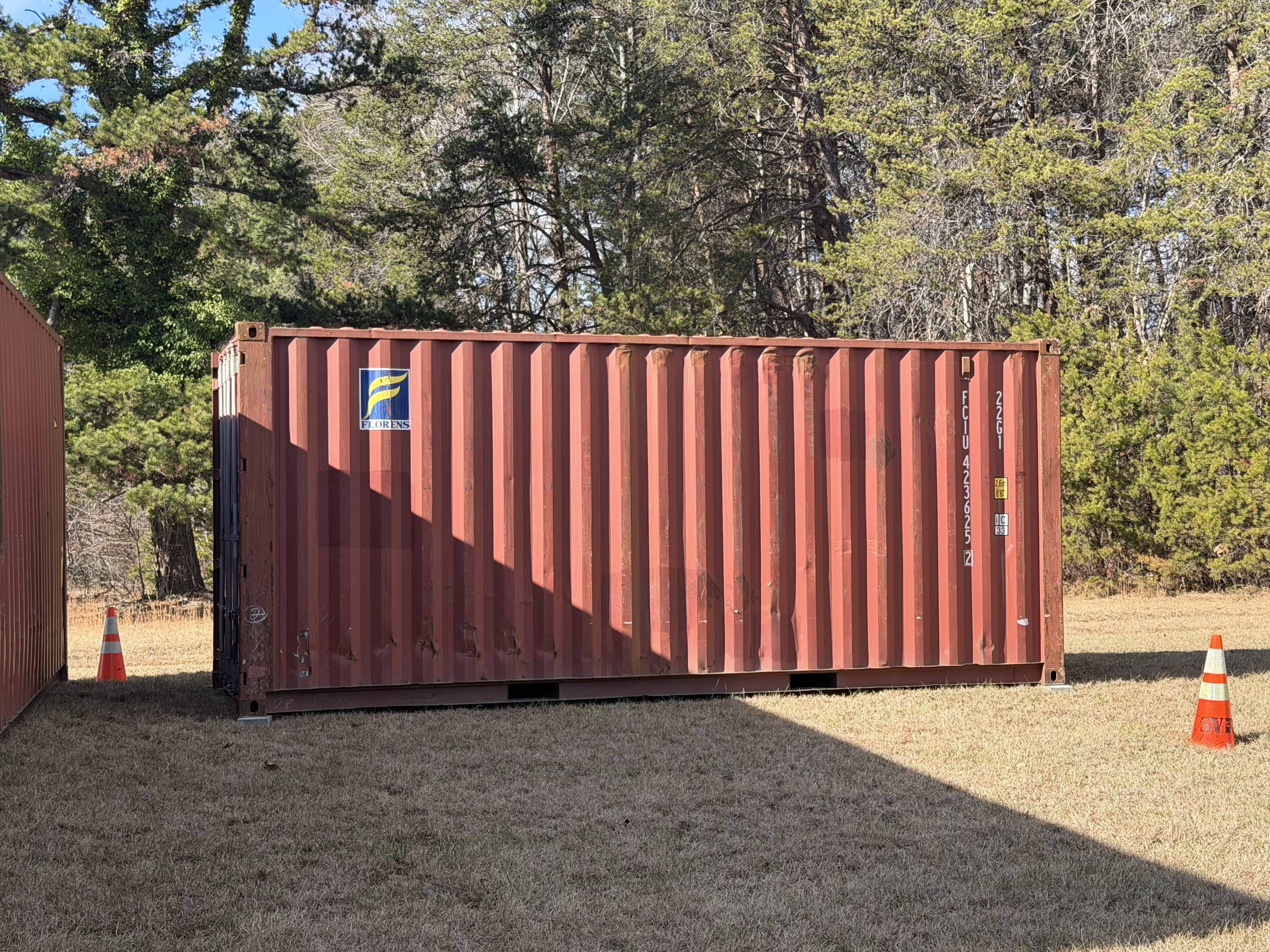 20 ft WWT shipping container, Florens Container Services, dark red paint, delivered to rural property with gravel pad, door end visible