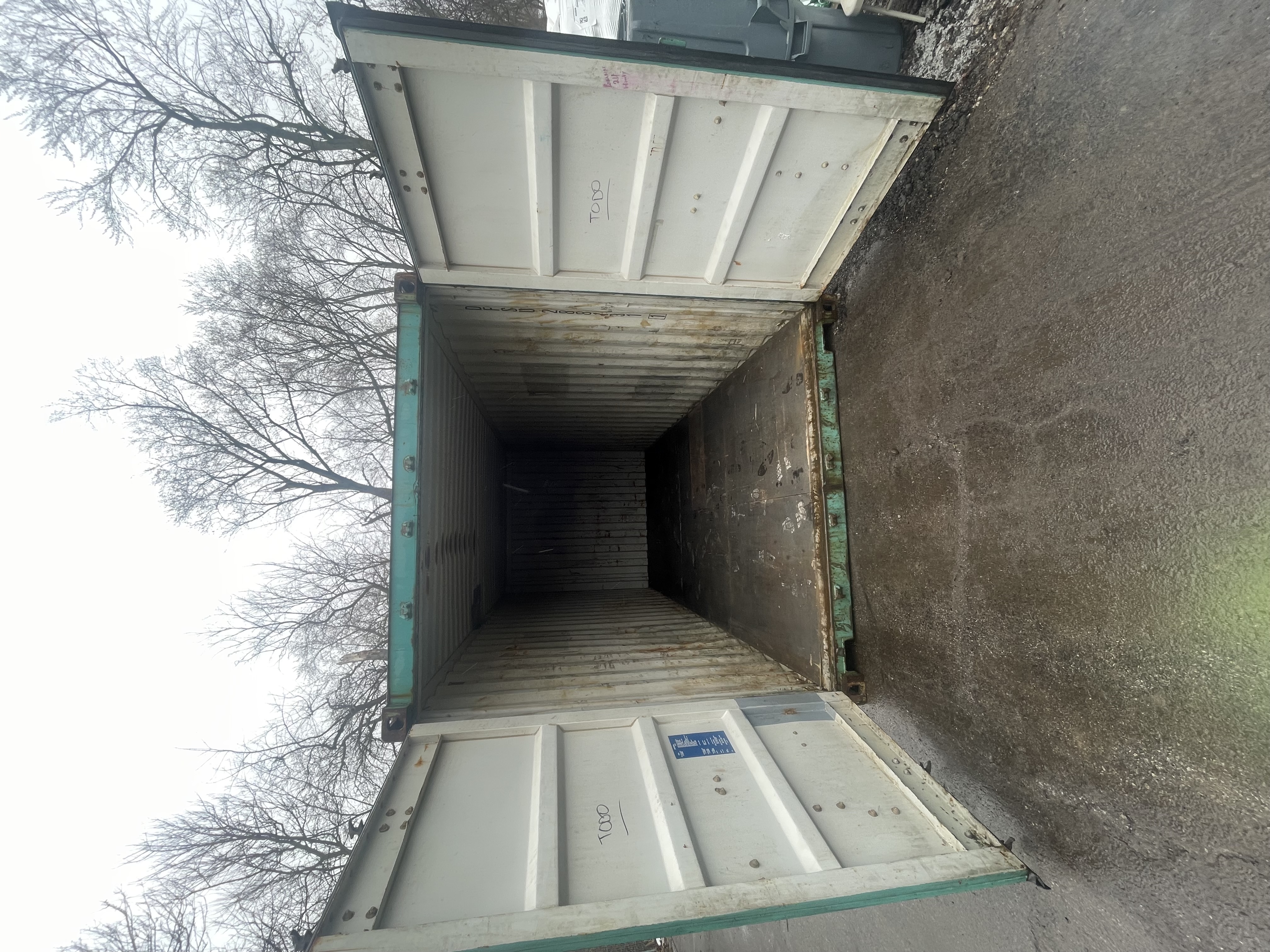 Interior of a 20 ft WWT shipping container, doors open, showing corrugated steel walls and worn wood flooring, teal corner castings