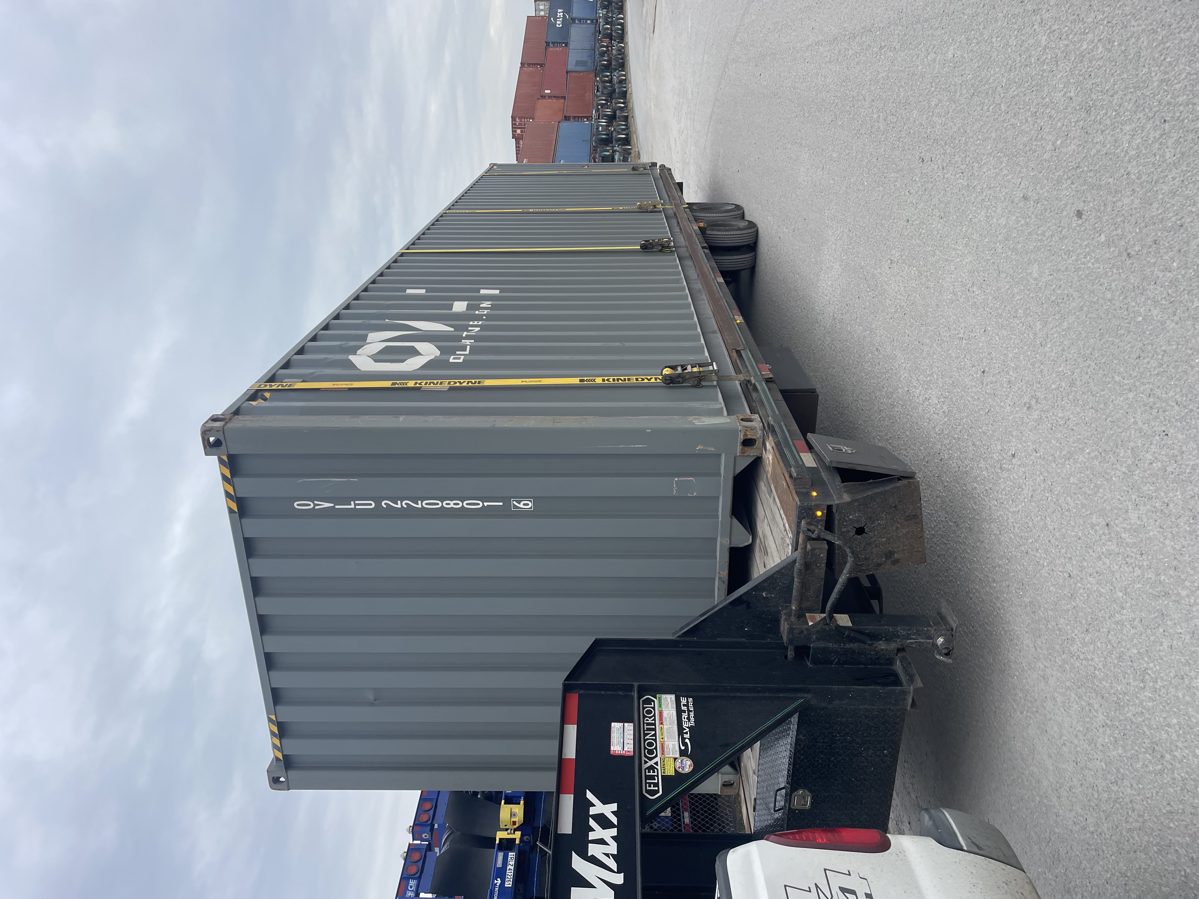 Grey Premium Multi-Trip shipping container secured to a gooseneck trailer for pickup