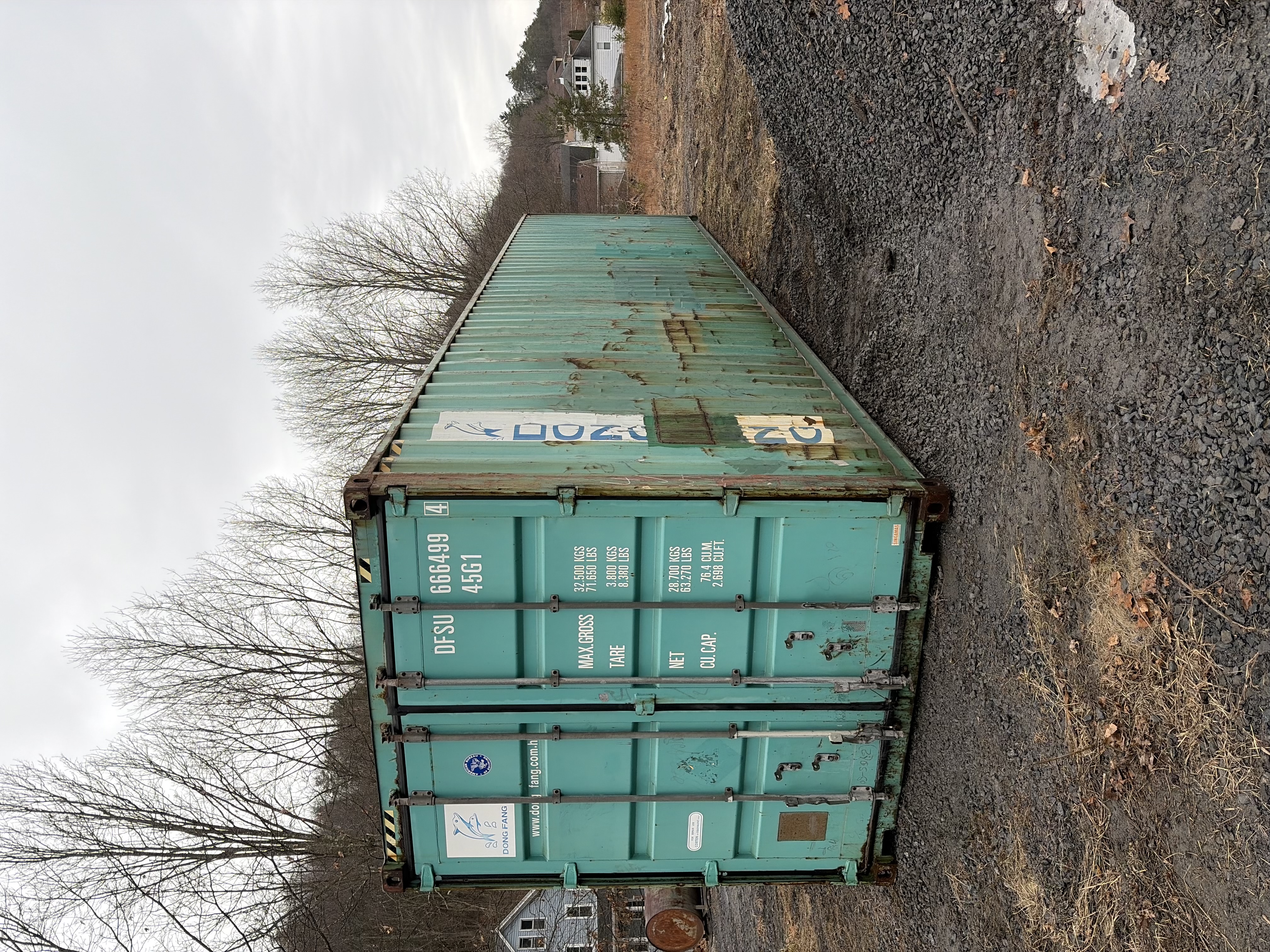 40 ft High-Cube WWT shipping container, Dong Fang livery, teal green paint with significant surface rust, delivered to gravel yard