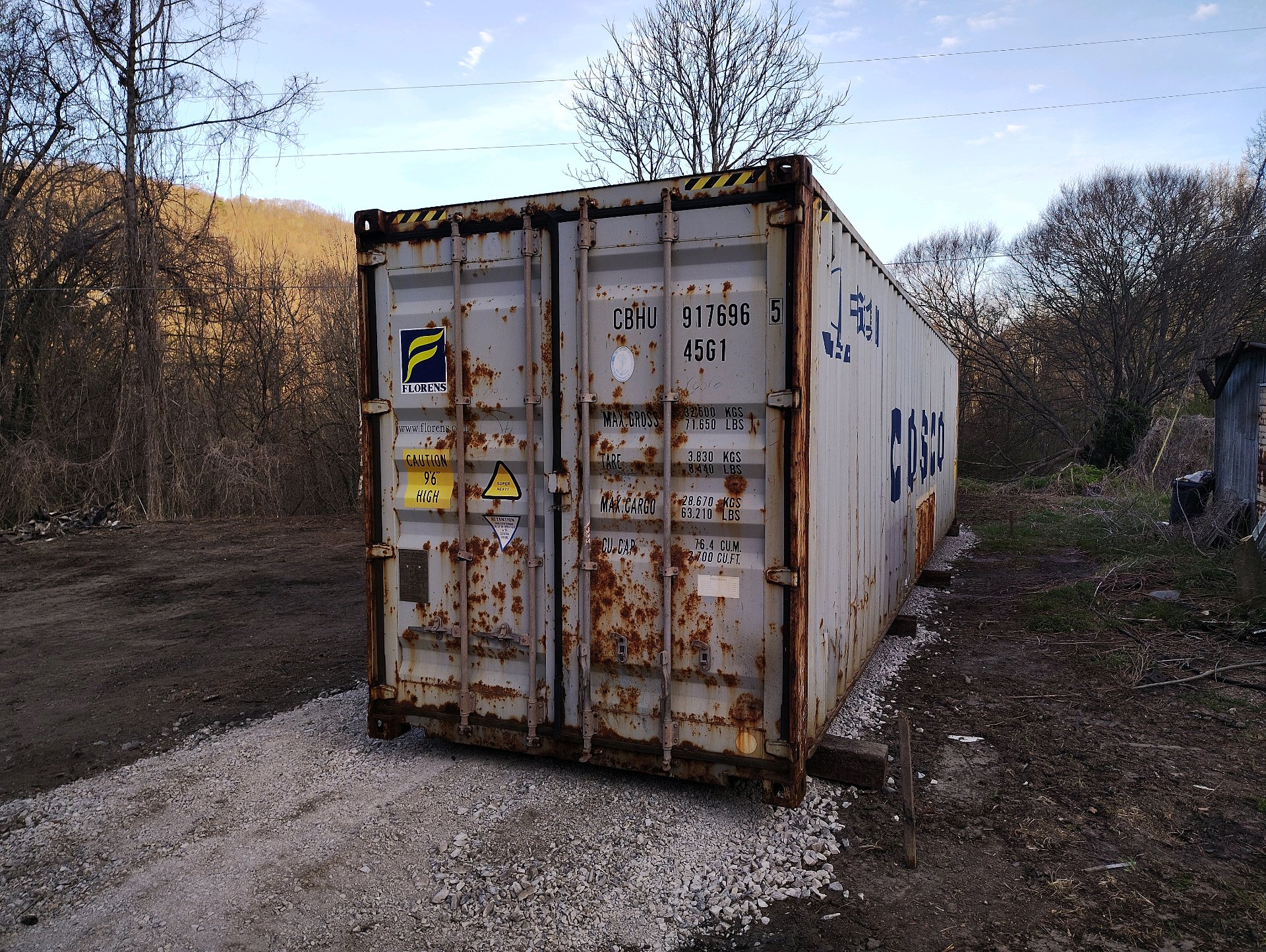 40 ft High-Cube WWT shipping container, Florens and COSCO markings, white paint with heavy surface rust on door end, delivered to rural property